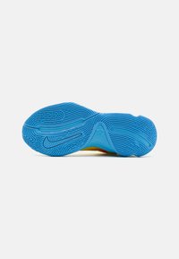 Sål af sko med en struktureret blå gummioverflade, der har buede dækmønstre og Nike-branding på mellemsålen. Lyse detaljer synlige.