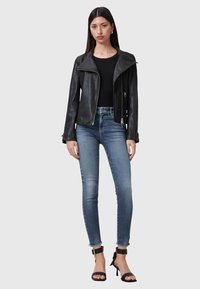 Czarna skórzana kurtka motocyklowa z ukośnym zamkiem, w połączeniu z jasnoniebieskimi obcisłymi dżinsami i czarnymi sandałami na obcasie. Gładka faktura, bez wzorów.
