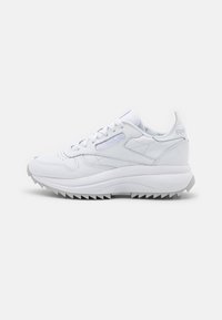 Baskets blanches en cuir de la marque Reebok avec fermeture à lacets et semelle en caoutchouc dentelée, présentées de profil sur un fond blanc.