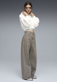 Sweat à capuche blanc oversize et court avec une fermeture éclair, associé à un jean gris taille haute à jambes larges et des chaussures argentées métalliques. Textures lisses.