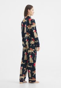 Granatowy zestaw piżamowy z wzorem lampartów i świątecznymi czapkami, wykonany z miękkiego materiału. Długie rękawy i luźne spodnie z czerwonymi akcentami.