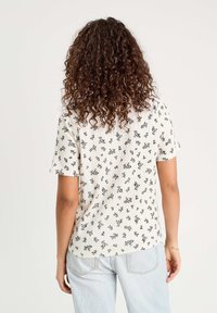 Short-sleeve top in cream with a ribbed texture, featuring a black floral pattern. Slightly rounded hem at the back, casual fit.