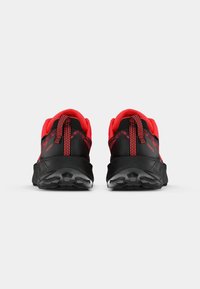 Une paire de chaussures de sport noires et rouges vue de l'arrière, montrant des cols rembourrés et des semelles extérieures en caoutchouc texturé.