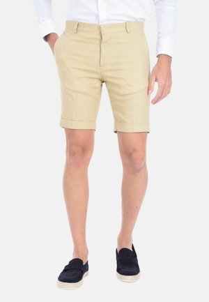 Pantaloni corti beige in lino con frontale piatto, risvolti e tasche laterali, abbinati a scarpe blu scuro slip-on.