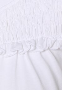 Vitt tyg med samlad smockdetalj och volangkant, som visar en mjuk textur och en jämn, enhetlig yta.