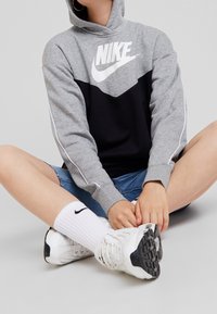 Sudadera con capucha de Nike en gris y negro con logo blanco, diseño con capucha y líneas limpias. Combinada con pantalones cortos de mezclilla, calcetines blancos y zapatos deportivos.