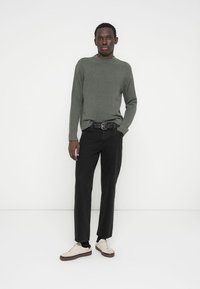 Camisola cinza de malha, calças pretas, cinto preto e sapatilhas brancas. Textura lisa, design justo, com decote redondo e estilo minimalista.