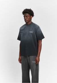 Schwarzes Gradient-Crewneck-T-Shirt aus weichem Stoff, mit kurzen Ärmeln und einem kleinen weißen Logo. Kombiniert mit passenden, lockeren schwarzen Hosen.
