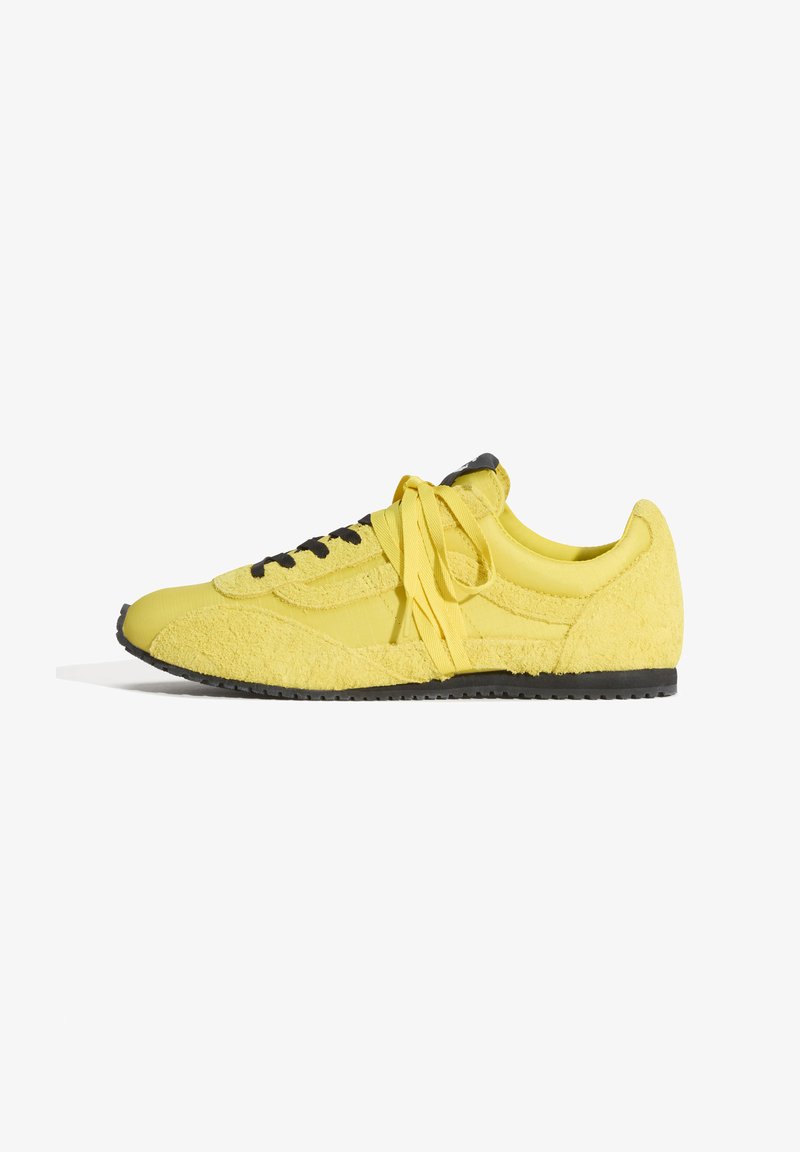 Baskets basses jaunes avec semelle noire et œillets noirs, dotées de tissu lisse et texturé et de lacets jaunes noués, vues de profil.
