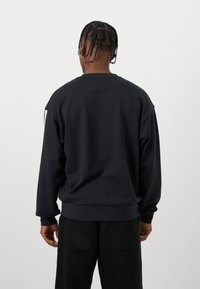 Svart hettegenser med avslappet passform, ribbede mansjetter og kant, og en glatt tekstur; har et hvitt aksent på skuldren.