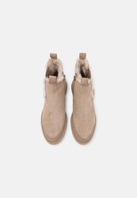 Botines beige de ante con textura suave, que cuentan con un forro de piel sintética, cremalleras laterales y tiradores en forma de lazo.