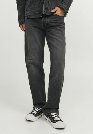 Jeans de denim negro con un corte recto, combinados con zapatillas negras y blancas. La tela tiene una textura, y los jeans cuentan con bolsillos estándar.