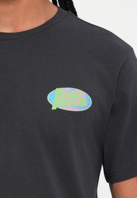 Sort bomulds t-shirt med rund halsudskæring, der har et flerfarvet logo, som står "Rivival Projects" på venstre bryst.