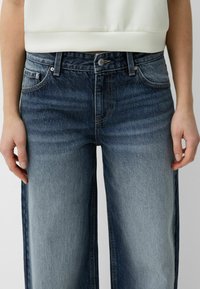 Jeans med vida ben i mörkblå färg med ljusare blekta områden, utrustade med fem fickor och knäppning. Materialet är mjukt, texturerat denim.