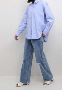 Camicia azzurro chiaro con un taglio morbido e maniche lunghe, abbinata a jeans in denim a gamba larga e strappati e sandali bianchi con tacco aperti.