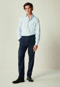 Lichtblauwe met patroon lange mouw knopsluiting shirt, marineblauwe geplooide broek en zwarte dresschoenen, weergegeven tegen een neutrale achtergrond.
