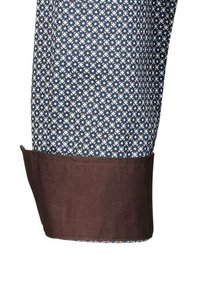 Manica di camicia con bottoni caratterizzata da un motivo a righe blu navy e bianco con un polsino marrone a contrasto. Il tessuto appare liscio con una forma strutturata.