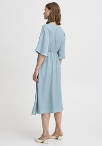Himmelblaues Midikleid mit tailliertem Bund, ausgestellten Ärmeln und weichem Stoff. Das Kleid hat eine schlichte, fließende Silhouette und ist knöchellang.