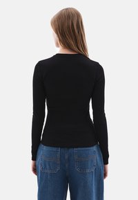 Schwarzes Langarmoberteil aus geripptem Stoff, tailliert, kombiniert mit hochgeschnittenen blauen Jeans mit genähten Taschen.