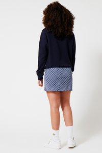 Navy sweatshirt with a relaxed fit, paired with a blue patterned mini skirt featuring diamond shapes. White sneakers and socks complete the outfit.