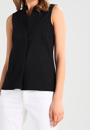 Top noir sans manches avec un décolleté en V, présentant une silhouette épurée et une texture douce. Associé à un pantalon blanc pour créer un contraste.