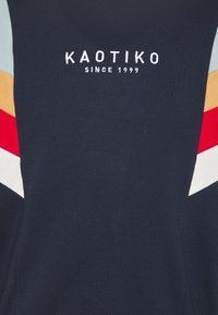 Felpa blu navy con un design a strati caratterizzato da motivi a zig zag in rosso, bianco, azzurro e arancione, e logo ricamato "KAOTIKO".