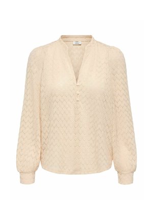 Blouse beige à manches longues avec motif hexagonal texturé, manches légèrement bouffantes, encolure en V et trois petits boutons à l'avant.