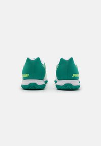 Des chaussures de sport en maille verte avec des accents blancs, présentant un dessus texturé et une semelle en caoutchouc, affichant "ATTACKCOURT" en jaune vif.
