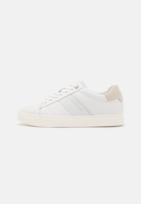 Sneakers in pelle bianca con texture liscia, caratterizzati da un tacco in suede beige, strisce tonali e lacci bianchi. Design minimalista con dettagli brandizzati.