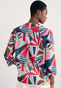 Mehrfarbige Bluse aus leichtem Stoff mit einem abstrakten geometrischen Muster in Rot, Blau, Pink und Braun, mit Dreiviertelärmeln.