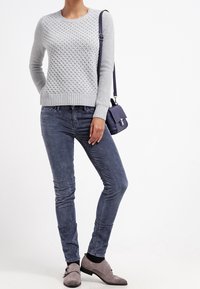 Grå texturerad tröja med rund halsringning, kombinerad med slim-fit blå jeans, grå skor och en liten mörk handväska.