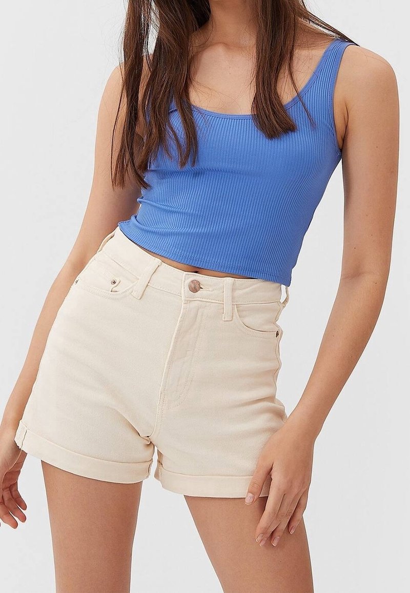 Camiseta de canalé azul claro combinada con shorts de mezclilla crema de tiro alto, con puños doblados y bolsillos delanteros, sobre un fondo liso.