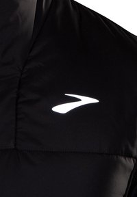 Schwarze Steppweste mit glänzender Oberfläche, gestepptem Muster und reflektierendem Logoakzent auf der linken Brustseite.