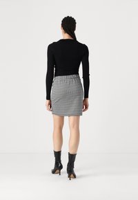 Fekete bordás hosszúujjú felső, amelyet egy fitted houndstooth mini szoknyával párosítanak. A modellen térd hosszúságú fekete magassarkú csizmák vannak. Egyszerű fehér háttér.