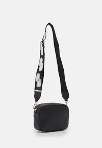 Černá crossbody taška z texturované kůže se zlatým zipem. Obsahuje kontrastní popruh s logem v bílé a šedé barvě, nastavitelné na délku.