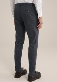 Marinblå mönstrade byxor i texturerad tyg, med en bakficka med knäppning, som matchas med mörkbruna skor.