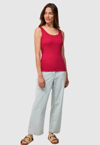 Top rojo de tirantes con escote redondo combinado con jeans de pierna ancha en azul claro. El modelo lleva sandalias marrones con tiras. Diseño simple y ajustado.