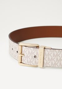 Weißer und brauner Leder-Gürtel mit "MK"-Muster, goldfarbener Metallschnalle und verstellbaren Löchern für die Größenanpassung. Glatte Textur mit fester Struktur.
