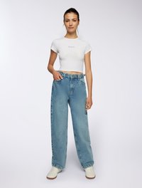 T-shirt bianco corto con il testo "Grateful"; jeans in denim azzurro chiaro, vestibilità rilassata; sneakers bianche con dettagli perforati.