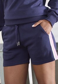 Marineblaue Baumwollshorts mit einem Kordelzugbund, Taschen an den Seiten und kontrastierenden vertikalen Streifen in Pink und Weiß an den Seiten.