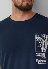 Donkerblauwe short-sleeve t-shirt van katoen, met een witte zeefdruk van een boomgrafiek op de boven-linkerzijde en de tekst "Omarm het Onbekende."