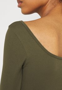 Maglietta a maniche lunghe ribbed verde oliva con scollatura ampia, caratterizzata da una texture liscia e una silhouette aderente.