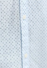 Ανοιχτό μπλε πουκάμισο με δύο κατακόρυφα χωριστά σχέδια, με μικρά σκούρα μοτίβα και λευκά κουμπιά κατά μήκος της κεντρικής ραφής.