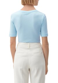 Ljusblå kortärmad topp i mjukt tyg, med rund halsringning och en figurnära design, tillsammans med krämfärgade byxor.