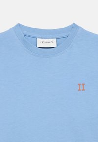 Světle modré bavlněné tričko s kulatým výstřihem a malou oranžovou výšivkou "II" na levé straně hrudi. Hladká textura, nenucený design.