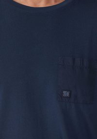 Marineblauwe t-shirt van zachte katoen met een ronde hals. Bevat een opgestikte zak aan de linkerkant, verfraaid met een logo-label.