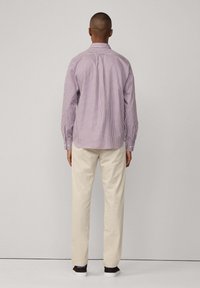 Camicia a maniche lunghe da uomo in un motivo a quadri rossi e bianchi, tessuto misto cotone, colletto con bottoni, schiena plissettata, indossata con pantaloni beige.