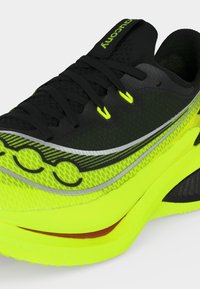 Μαύρο και νέον κίτρινο παπούτσι τρεξίματος με κορδόνια και επωνυμία στο πλάι, με παχύ, επενδεδυμένο πέλμα για υποστήριξη.