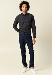 Camicia nera a maniche lunghe con bottoni, jeans in denim scuro e sneaker bianche. Denim a gamba dritta, con i risvolti arrotolati. Tessuto morbido.