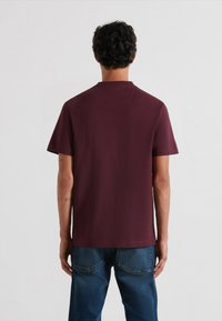 Maglietta a maniche corte bordeaux realizzata in tessuto morbido, con colletto rotondo e taglio dritto, abbinata a jeans in denim blu a vestibilità standard.